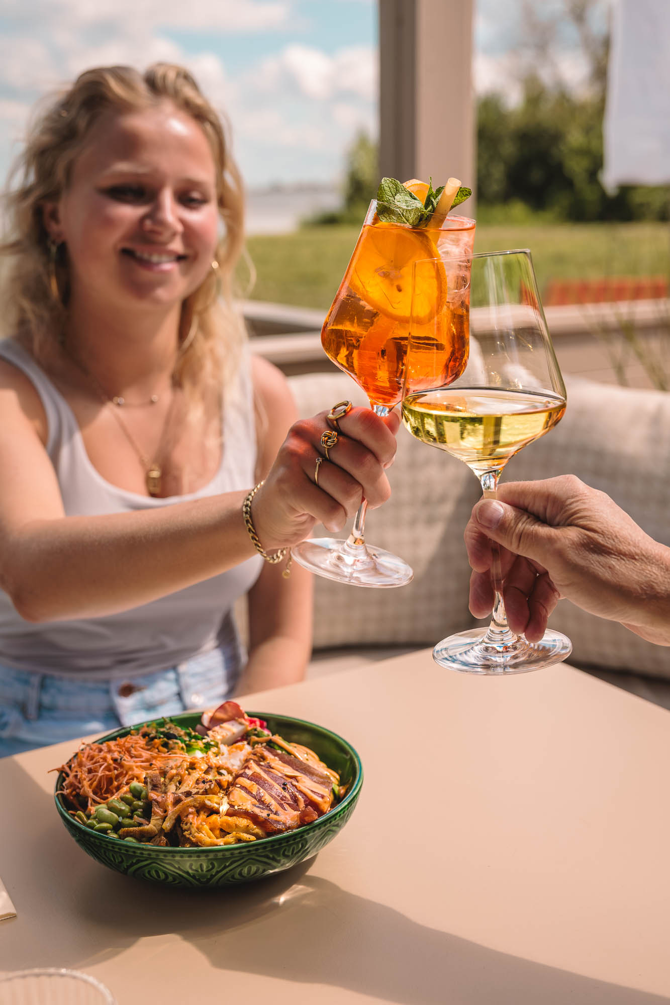 Gasten proosten op het terras van atMirror met een poké bowl